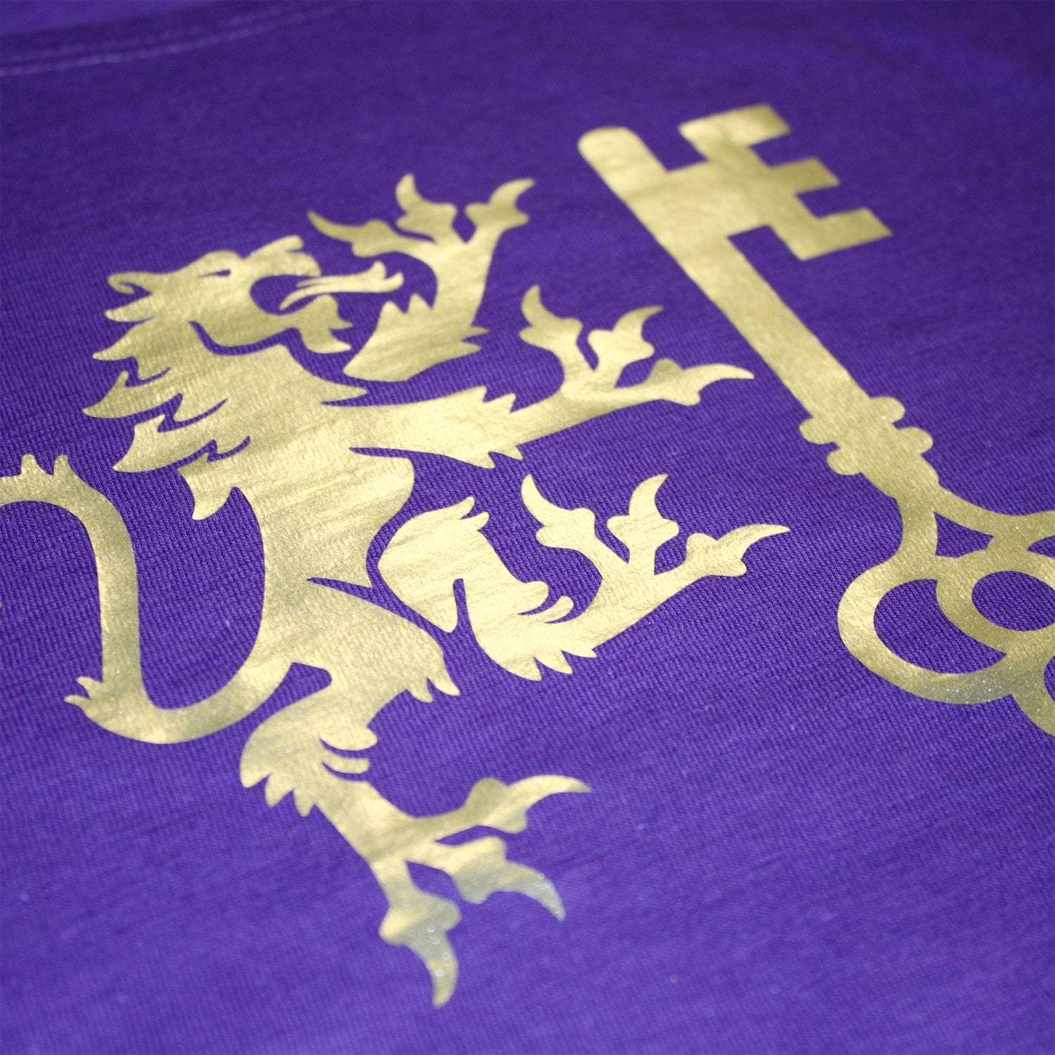 Goldener Löwe und Schlüssel bestickt auf lila Textil